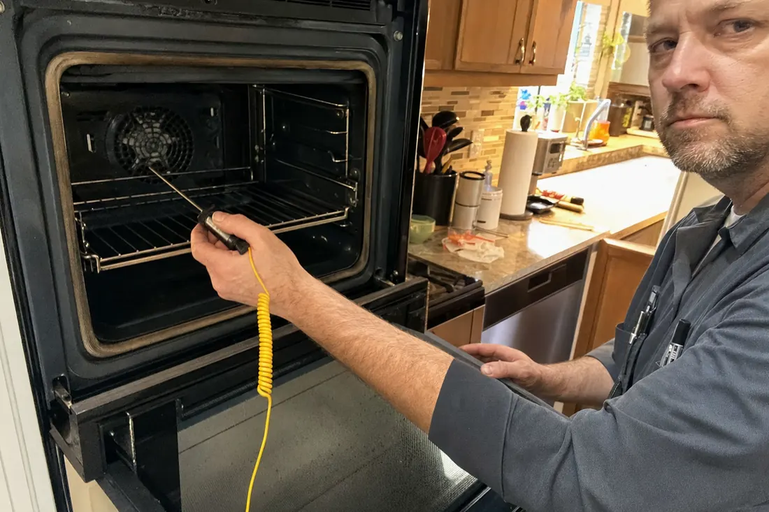 Technician holding a probe thermometer inside an open wall oven, the open door in frame - Thermador Repair Across the First Coast